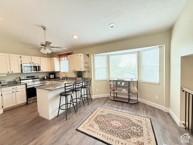 Kitchen featuring white cabinetry, stone-finish countertops, stainless steel appliances, a center island with bar seating, and a bay window