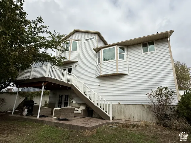 Multi-level exterior featuring light-toned vinyl siding, bay windows, an elevated deck with white railings, and a stamped concrete patio