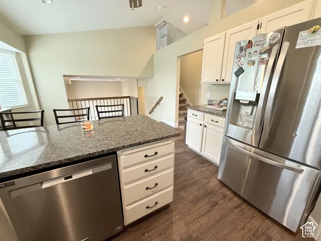 Kitchen featuring stone-surface countertops, white cabinetry with dark hardware, stainless steel appliances, wood-finish flooring, and vaulted ceilings
