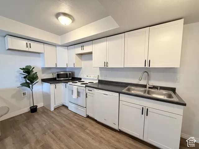 Kitchen featuring white cabinetry with dark hardware, dark countertops, a double-basin stainless steel sink, a pull-down faucet, and wood-finish flooring