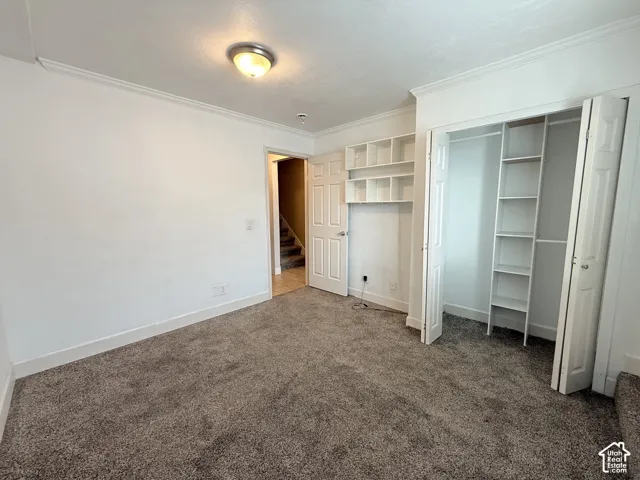 Room featuring neutral carpeting, crown molding, built-in wall shelving, and a closet with integrated storage