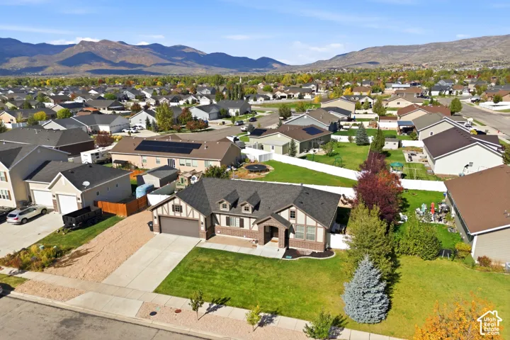 Aerial perspective of a single-story residence featuring a brick and paneled exterior, an attached two-car garage, a concrete driveway, and a manicured front lawn with mountain surroundings
