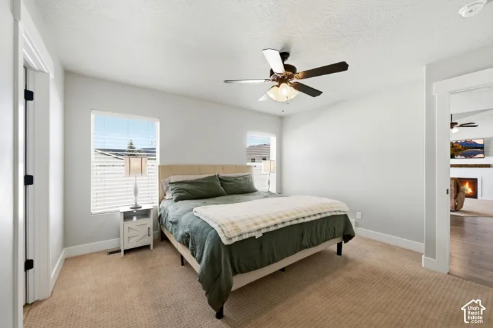 Neutral-toned interior featuring wall-to-wall carpeting, dual windows with integrated blinds, and a multi-blade ceiling fan with an integrated light fixture