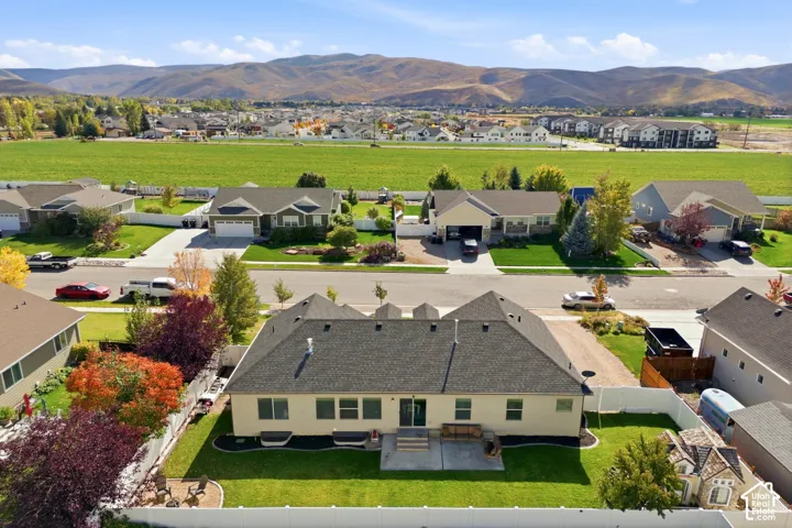 Aerial view of residence featuring a rear concrete patio, fully enclosed perimeter fencing, manicured lawn, and mountain scenery