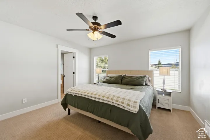 Neutral-toned room featuring wall-to-wall carpeting, dual windows with blinds, and a multi-blade ceiling fan with an integrated light fixture