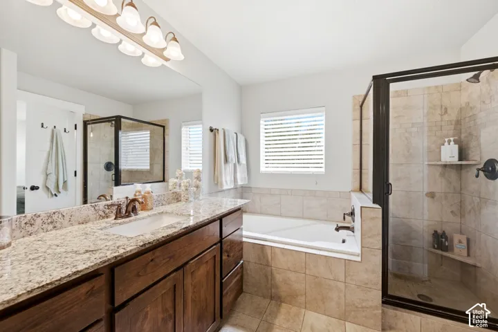 Bathroom featuring a vanity with stone-surfaced countertop, wood-finish cabinetry, a large wall-mounted mirror, a deep soaking tub, and a glass-enclosed shower with tiled surround