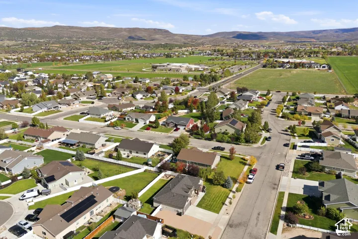 Aerial perspective of a suburban community featuring residential homes, paved streets, manicured lawns, white vinyl fencing, and a mountainous horizon