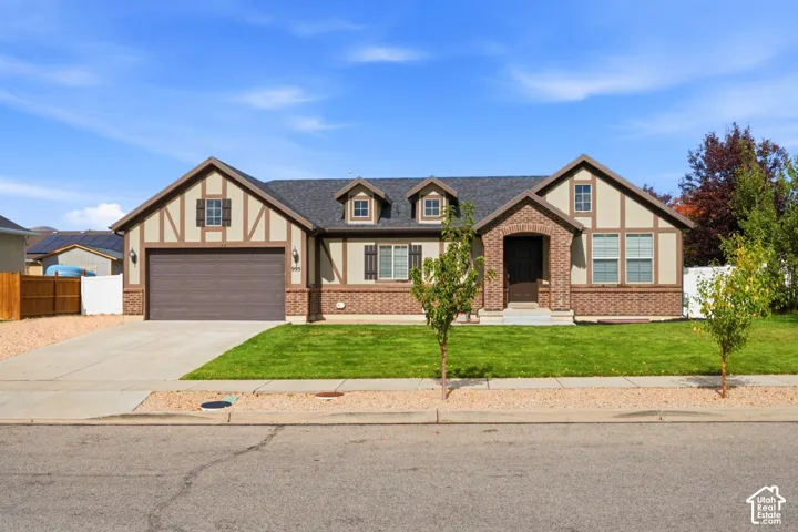 Tudor-inspired exterior featuring brick and stucco siding, a multi-gabled roofline with dual dormers, arched masonry entry, and a concrete driveway