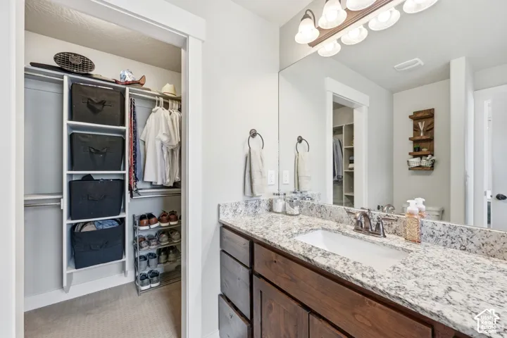 Vanity featuring a stone countertop, an integrated rectangular sink, wood-finish cabinetry, and a full-width mirror with integrated lighting
