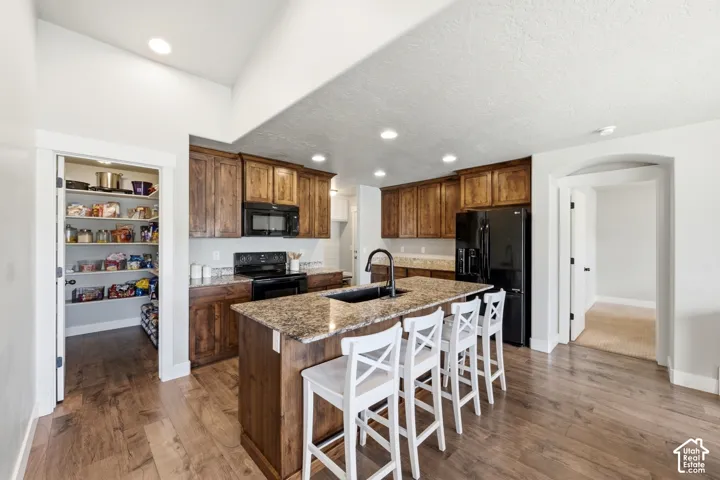 Kitchen featuring dark wood-finish cabinetry, an expansive central island with stone-finish countertop, integrated black appliances, recessed lighting, and an oversized walk-in pantry