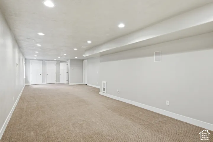 Expansive interior room featuring neutral wall paint, recessed lighting, carpet flooring, and multiple white panel doors