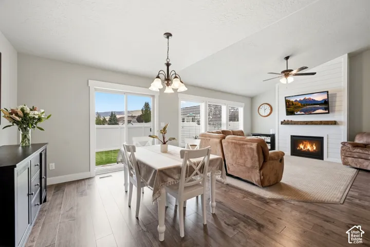 Living area featuring wood-finish flooring, white shiplap accent wall, fireplace with timber mantel, ceiling fan, and sliding glass door
