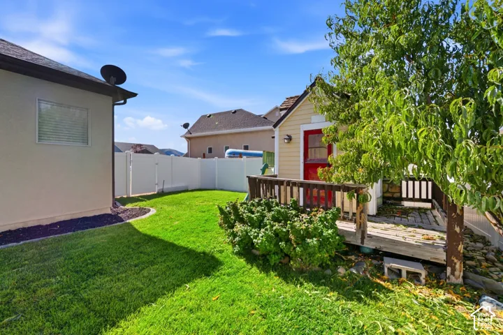 Backyard featuring a grass lawn, white vinyl fencing, a detached auxiliary structure with a wood deck, and stone ground cover