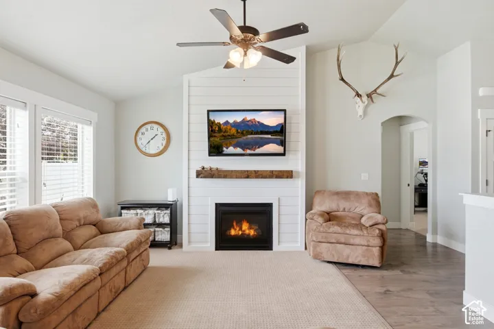 Vaulted ceiling featuring a white shiplap fireplace surround, a dark-toned wood-finish mantel, an integrated fireplace, and a ceiling fan with light fixture