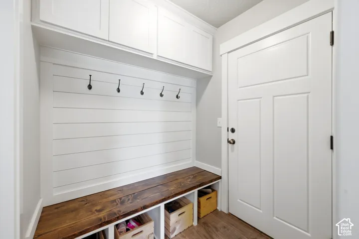 Built-in storage bench featuring a dark stained wood surface, white shiplap wall paneling, five mounted matte black hooks, and upper cabinetry