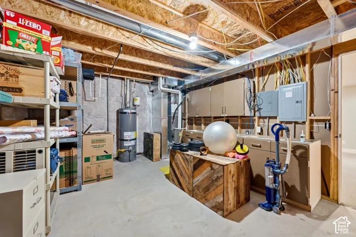 Unfinished utility area featuring exposed joist ceiling, concrete flooring, dedicated water heater, and wall-mounted cabinetry