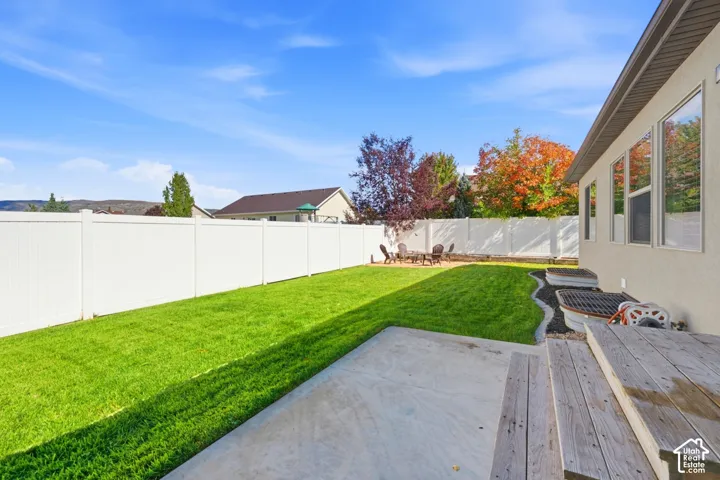 Fenced backyard featuring a manicured lawn, concrete patio, wood-finish stairs, and integrated window wells