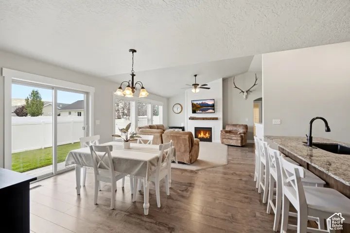 Open-concept interior featuring wood-finish flooring, a fireplace with a textured surround and natural wood mantel, sliding glass door, and a kitchen island with stone-finish countertop and matte black fixtures