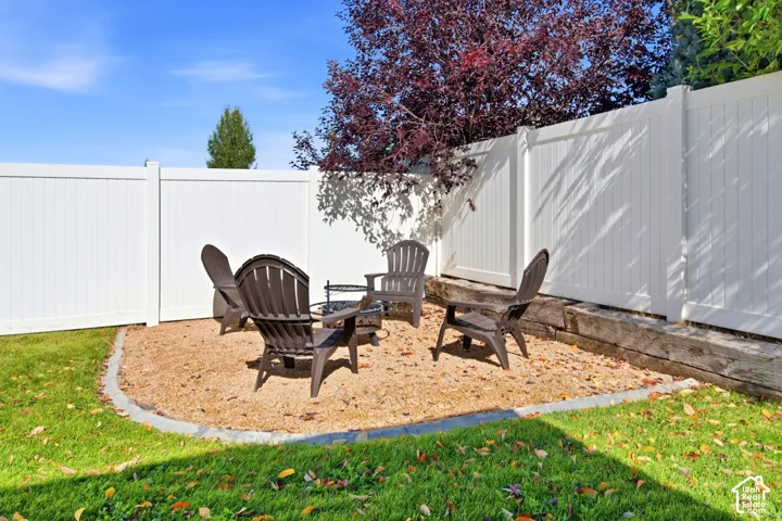 Backyard area featuring a gravel patio, stone border, timber retaining wall, and white vinyl privacy fencing