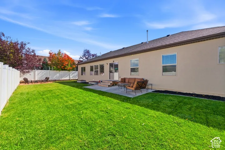 Rear exterior featuring a concrete patio, a fully enclosed vinyl fence, and a manicured lawn