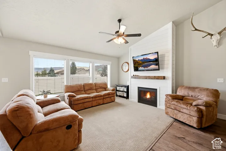 Living area featuring a vaulted ceiling, horizontal plank fireplace accent wall, rustic timber mantel, built-in fireplace, and expansive multi-pane windows