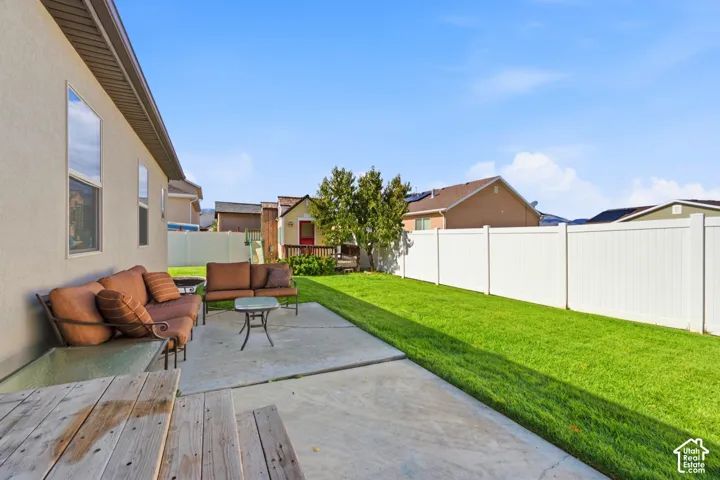 Rear exterior featuring a concrete patio, a grass lawn, and white vinyl perimeter fencing