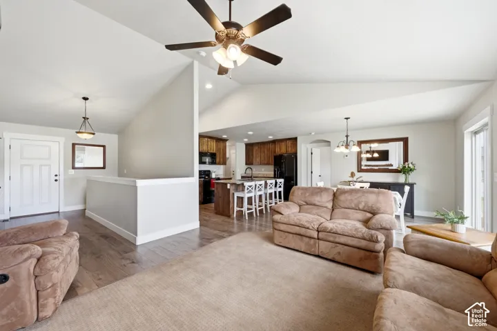 Vaulted ceilings, wood-finish flooring, kitchen island with built-in cabinetry, and multi-light pendant and ceiling fan fixtures