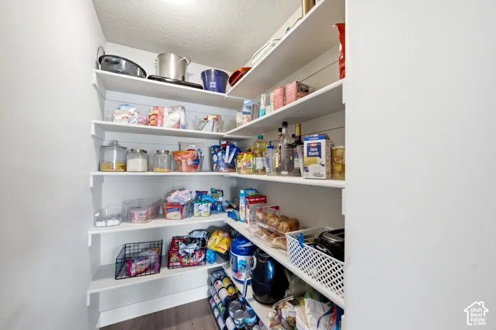 Walk-in pantry featuring multiple tiers of white shelving and wood-finish flooring