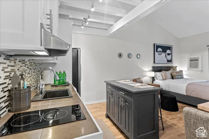 Kitchenette featuring a tiled countertop, stainless steel vent hood, mosaic tile backsplash, wood-finish flooring, and a dark-toned center island with storage