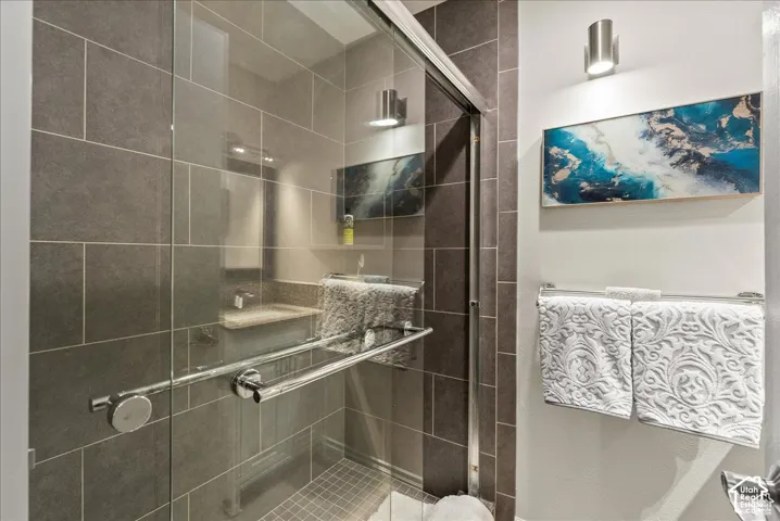 Walk-in shower with floor-to-ceiling tile, glass sliding doors, mosaic floor tiling, and integrated wall-mounted lighting
