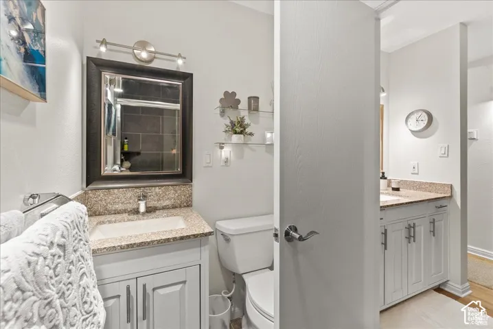 Dual vanity areas featuring light-toned cabinetry, speckled stone-composite countertops, rectangular undermount sinks, and brushed-metal hardware
