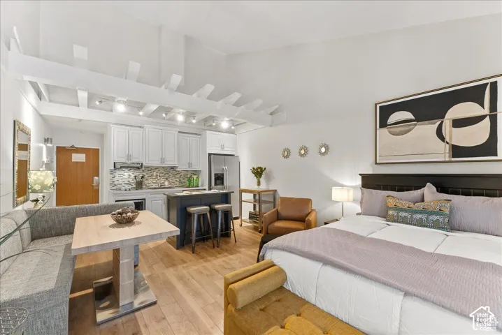 Vaulted ceilings with exposed structural beams, wood-finish flooring, white shaker cabinetry, decorative tile backsplash, and a central island with integrated seating
