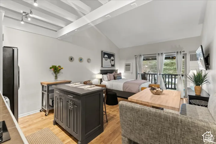 Vaulted ceilings with exposed beams, wood-finish flooring, and sliding glass doors providing outdoor access