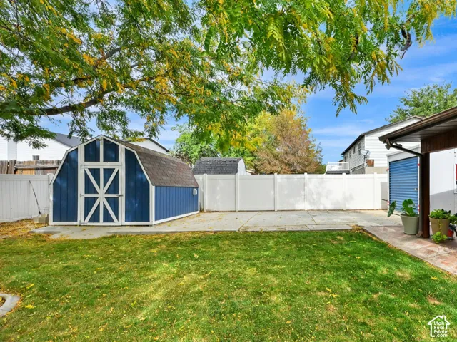 Expansive backyard featuring a manicured lawn, a blue barn-style shed, and a white privacy fence