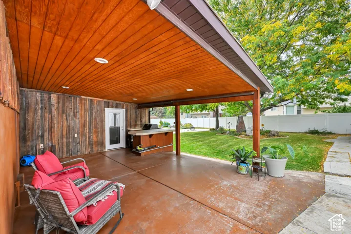 Covered patio with a wood-plank ceiling, wood-paneled exterior wall, built-in outdoor kitchen, and a concrete patio surface