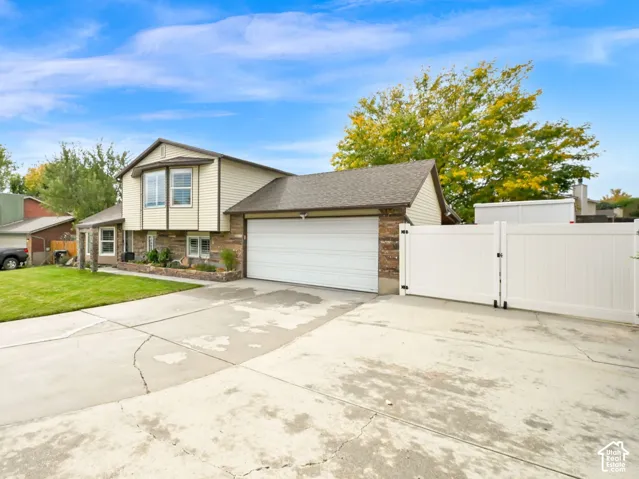 Split-level residence featuring a two-car garage, bay window, and a white privacy fence