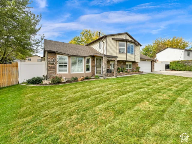 Split-level property featuring a stone and siding exterior, bay windows with plantation shutters, a two-car garage, and a manicured lawn