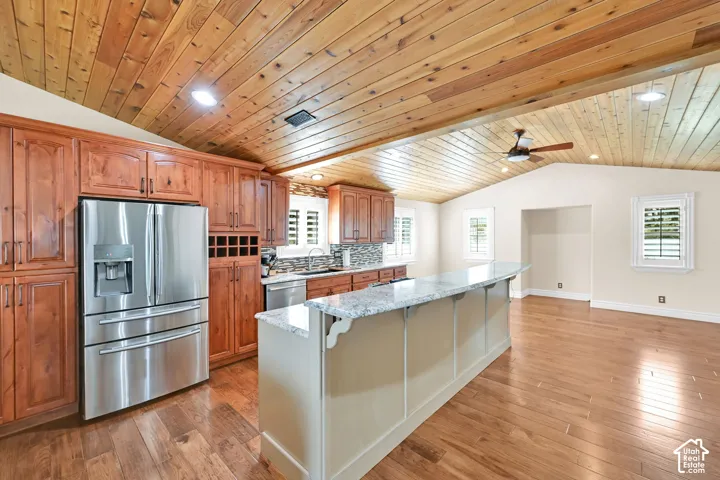 Vaulted wood-paneled ceiling, wood-finish flooring, full-height cabinetry, stainless steel refrigerator, and a kitchen island with stone countertop