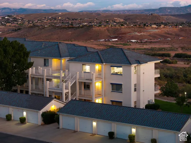Aerial: Twilight over Las Palmas, with the lit top-floor end unit looking out across open desert and red rock hills.