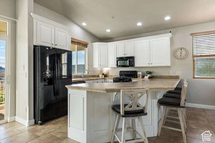 Kitchen: White cabinetry, a black side-by-side refrigerator, and a breakfast bar with room for four stools.