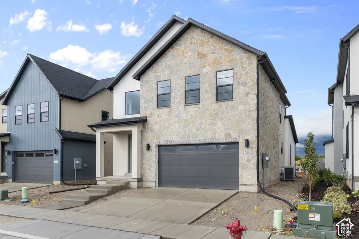 Multi-level exterior featuring a stone facade, vertical board-and-batten siding, concrete driveway, and attached two-car garage