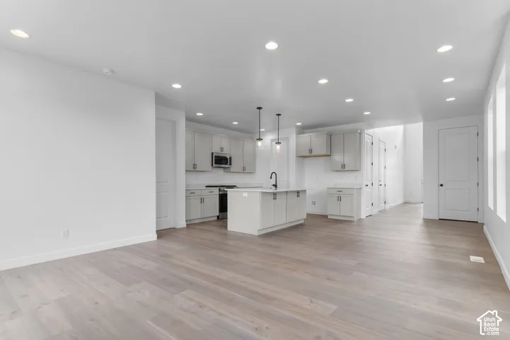 Open-concept kitchen featuring shaker-style cabinetry, an island with a matte black faucet, wood-finish flooring, and recessed ceiling lighting