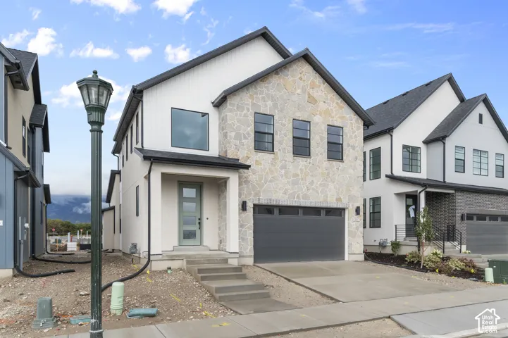 Two-story exterior featuring vertical siding, stone masonry veneer, a multi-pane glass entry door, and a two-car garage