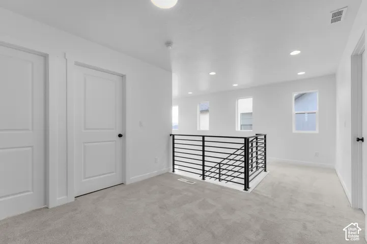 Open space featuring neutral carpeted flooring, recessed lighting, multi-panel interior doors with matte black hardware, and a black metal horizontal-bar railing