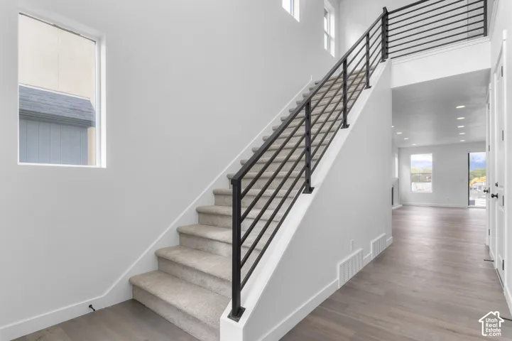 Staircase featuring a matte black metal railing and carpeted treads, complemented by wood-finish flooring, recessed lighting, and large windows