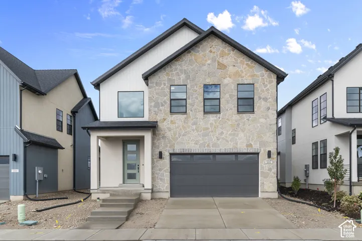 Two-story exterior featuring stone veneer facade, vertical siding, multi-pane windows, and a two-car garage