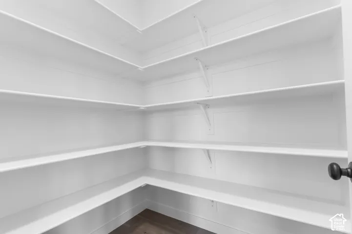 Storage space featuring multiple tiers of white wraparound shelving, white support brackets, and wood-finish flooring