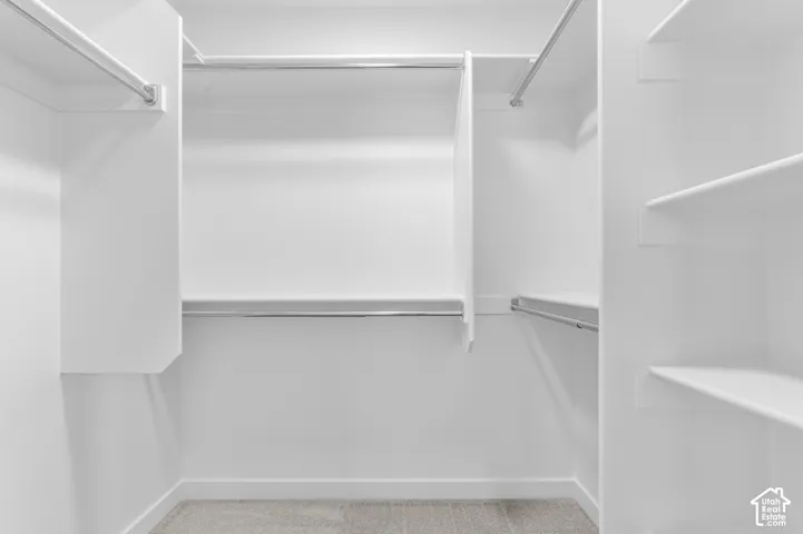 Walk-in closet featuring white built-in shelving, dual-level metal garment rods, and carpeted flooring
