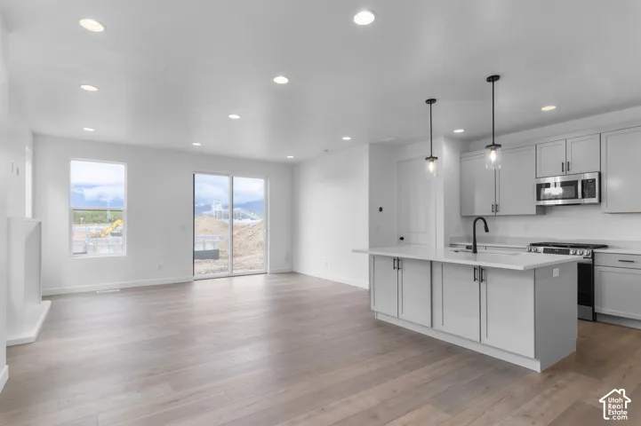 Kitchen featuring shaker-style cabinetry, a central island with a solid surface countertop, wood-finish flooring, recessed lighting, and pendant fixtures