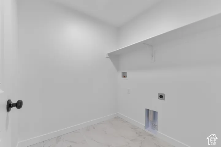 Utility room featuring light-toned stone-patterned tile flooring, a wall-mounted shelf, and dedicated water and electrical hookups
